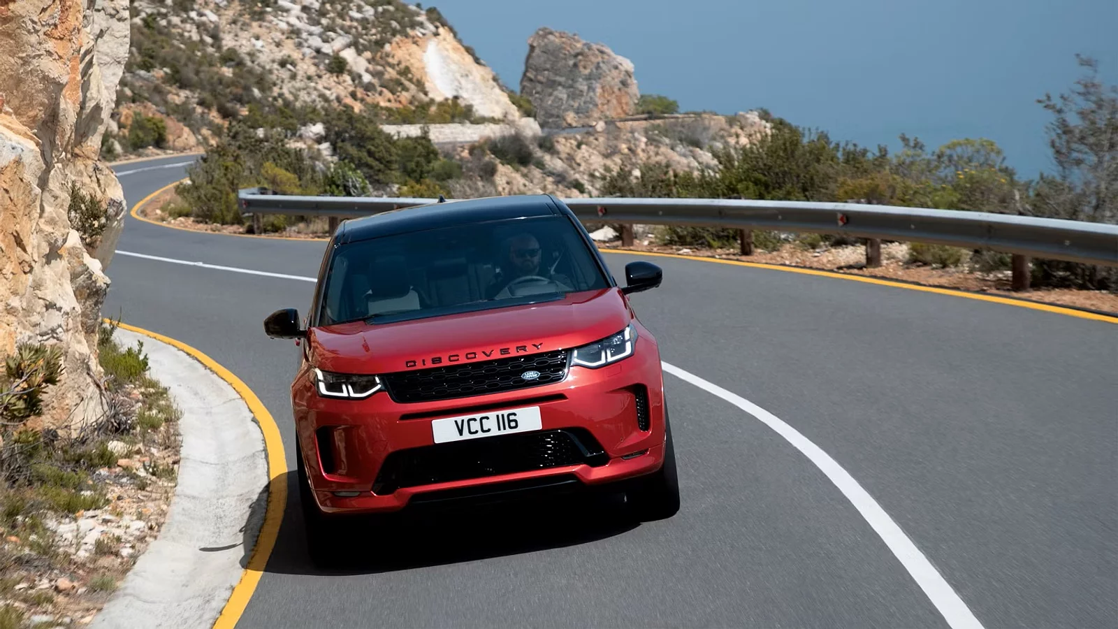 Discovery Sport rouge sur une route dégagée en montagne, conduit par un homme