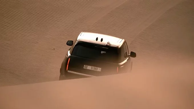 Range Rover towing a large, aerodynamic black enclosed trailer along a country road against a mountain backdrop.